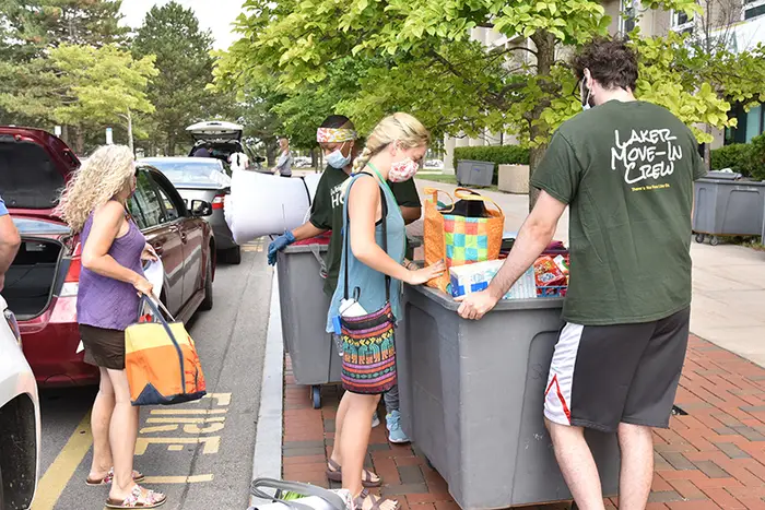 Students move into SUNY Oswego, with a cart and while wearing masks, on a campus sidewlak